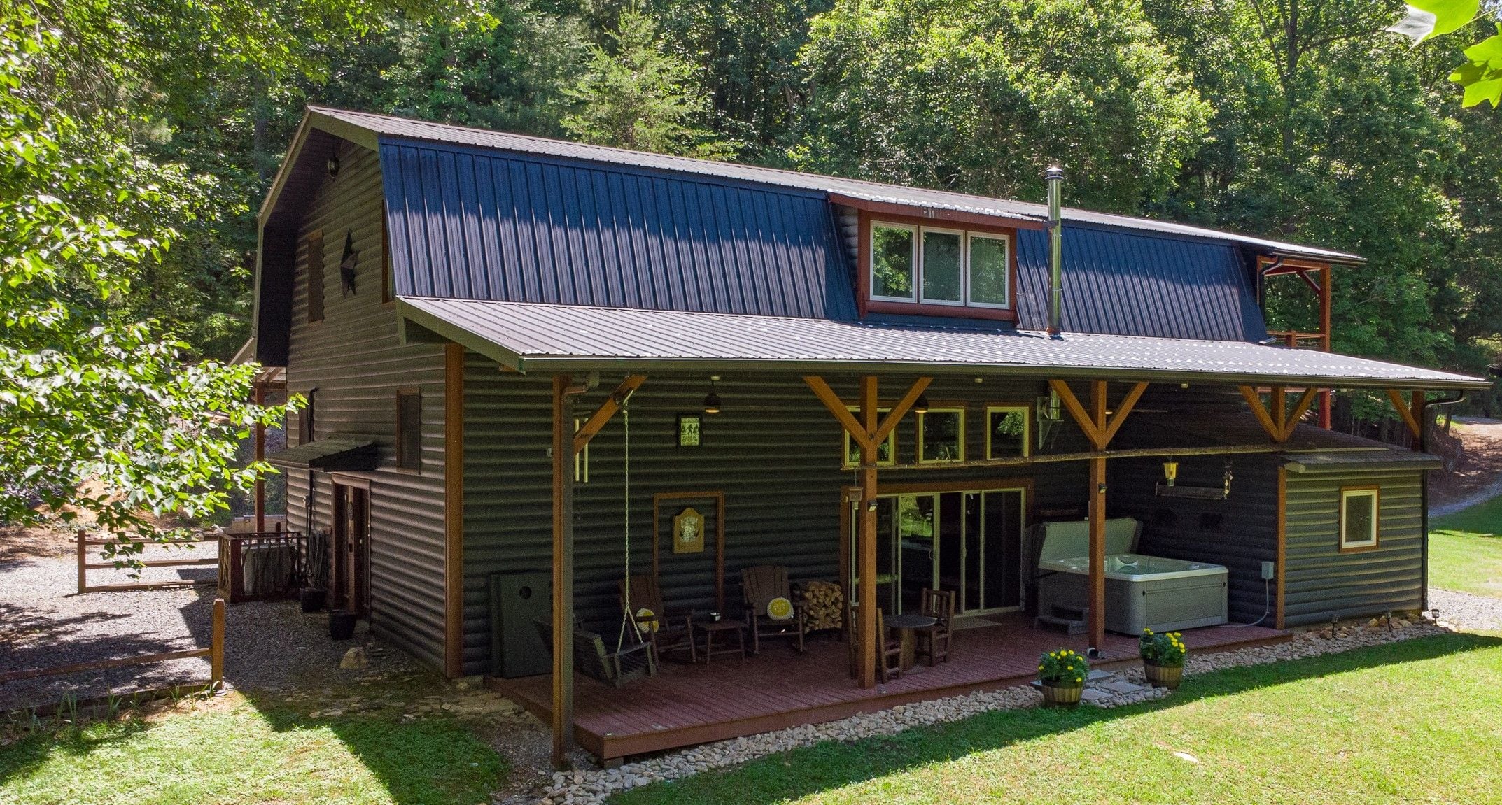 A two-story log cabin with a covered patio area, outdoor seating, and a large window.