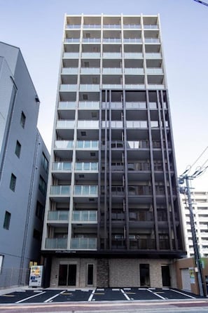 A multi-story hotel with a modern facade, a ground-level entrance, and a parking area in front. - Hotel Reference Tenjin III (Fukuoka)