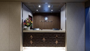 A hotel reception desk with a logo, a flower arrangement, and two laptops. - Hotel Reference Tenjin III (Fukuoka)