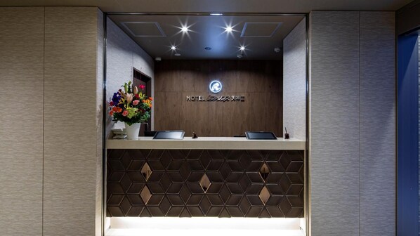 Una recepción de hotel con un logotipo, un arreglo floral y dos computadoras portátiles.