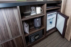 Un minibar pequeño con una cafetera, una taza y una botella.