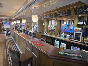 Zona de bar con diferentes opciones de asientos, una variedad de botellas de licor y una pantalla de televisión.