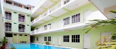 A multi-story building with a swimming pool, balconies, and doors.