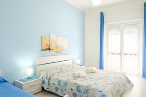 A bedroom with a bed, nightstands, a wall-mounted artwork, and a view through a door. - Apartment 'I Colori Del Mare' with Sea View, Wi-Fi and Air Conditioning (Lu Bagnu)