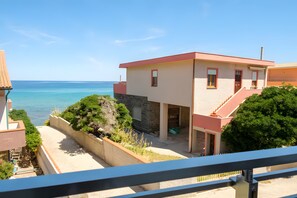 A coastal property with a view of the sea, a stone wall, and a balcony. - Apartment 'I Colori Del Mare' with Sea View, Wi-Fi and Air Conditioning (Lu Bagnu)