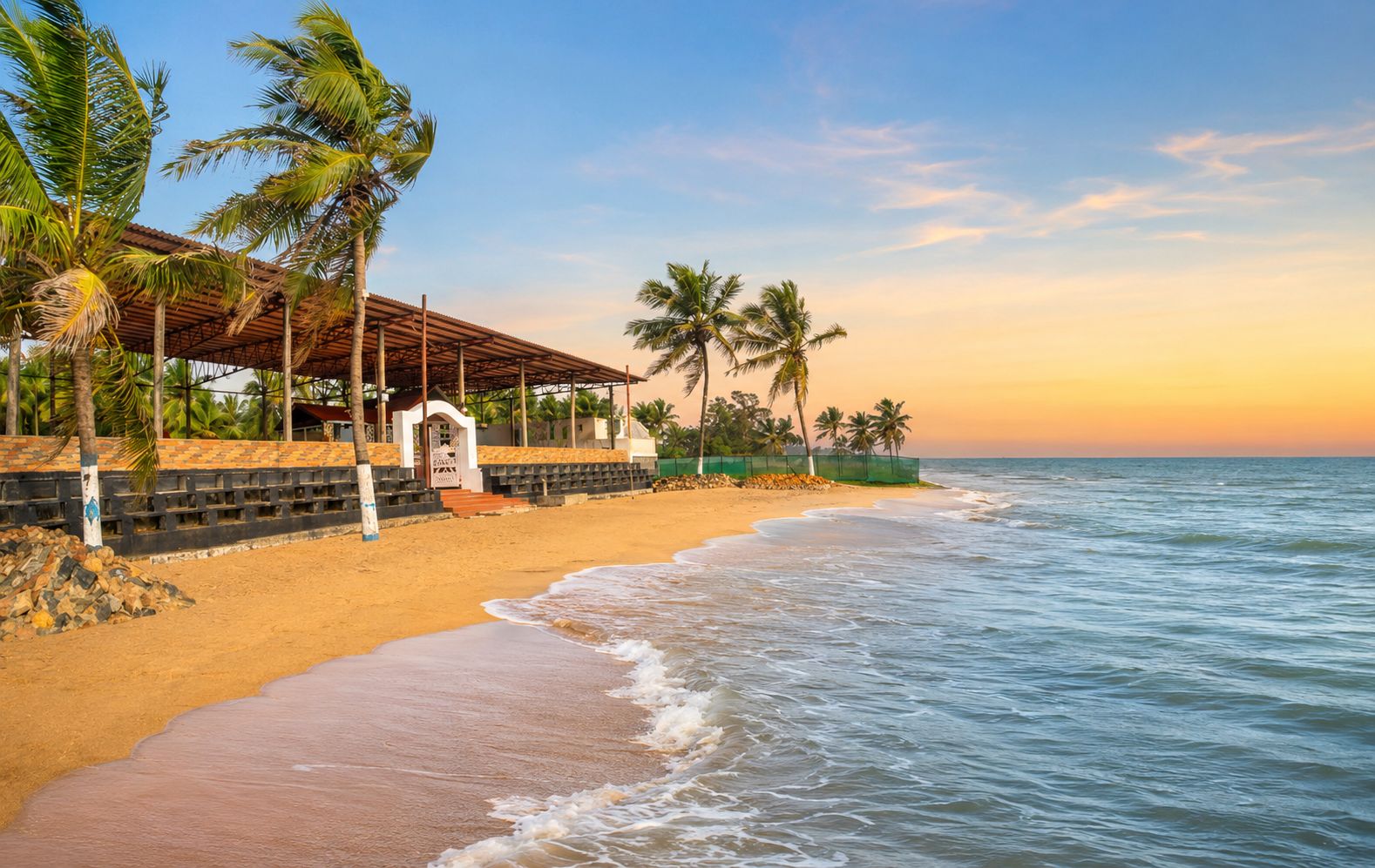 Una playa con zona de estar cubierta, palmeras y vistas al océano.