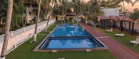 A swimming pool surrounded by palm trees and lounge chairs, with a building in the background.