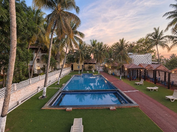 A swimming pool surrounded by palm trees and lounge chairs, with a building in the background.