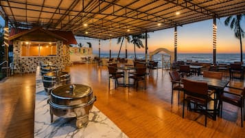 Un restaurante con terraza frente al mar, que presenta suelo de madera, ollas de metal para servir y una pared de piedra con un mural.