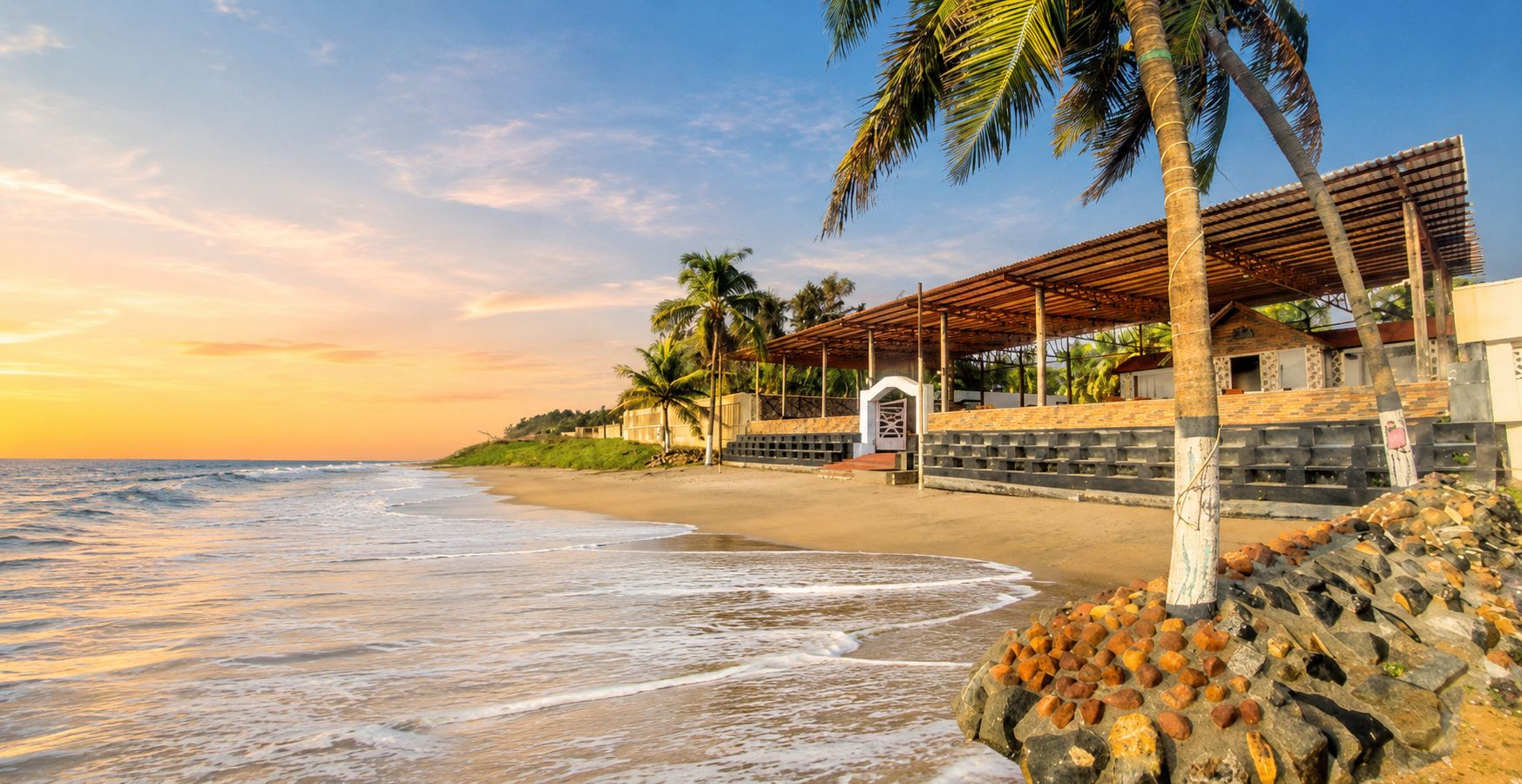 A beach with a wooden structure, palm trees, and a clear sky.