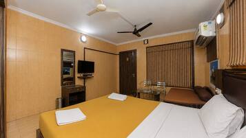 A hotel room with a bed, a television, a desk with chairs, and a ceiling fan.