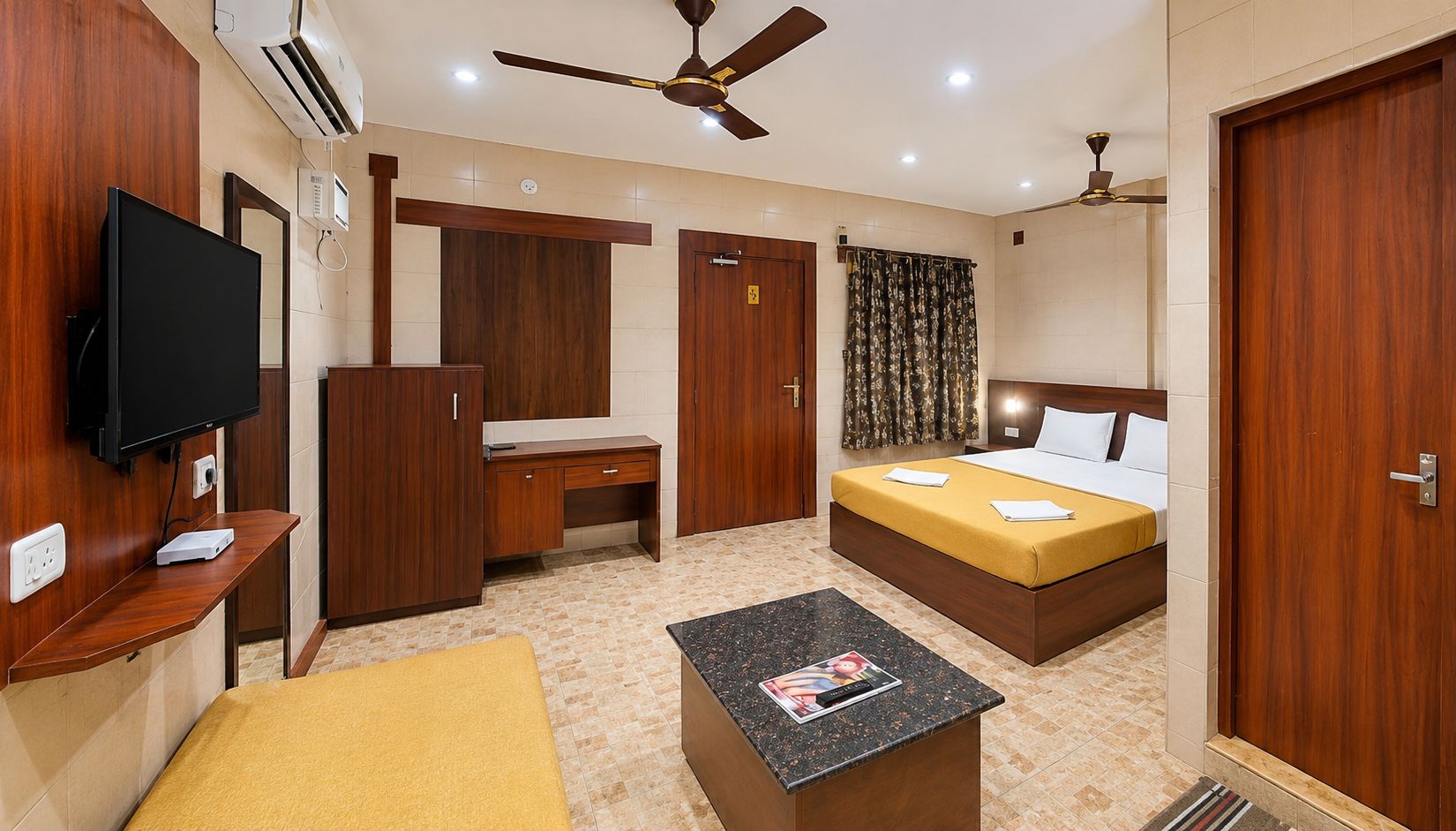 A hotel room with a bed, a desk, a television, and a ceiling fan.