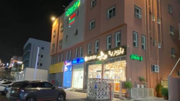 Un hotel de varios pisos con un letrero llamativo, un espacio al aire libre cubierto y un estacionamiento.