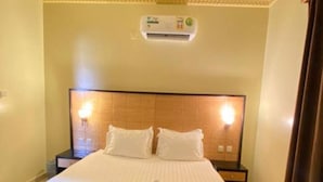 Una habitación de hotel con una cama grande, una mesita de noche, un aire acondicionado instalado en la pared y un candelabro colgante.