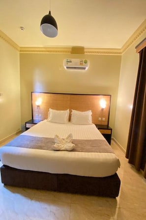 Ein Hotelzimmer mit einem großen Bett, einem Nachttisch, einer Wand-Klimaanlage und einer Hängeleuchte.