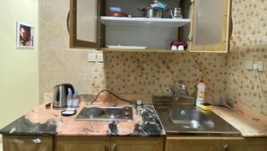 Una cocina con encimera de mármol, armarios de madera, un lavamanos doble y un pequeño estante abierto sobre el fregadero.