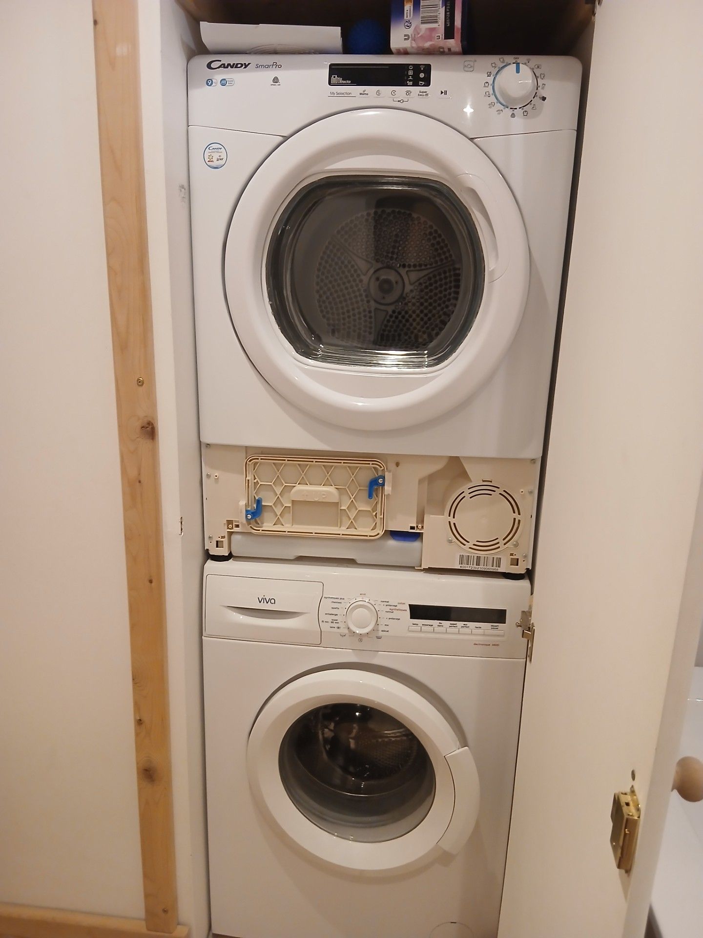 Un appareil compact combinant lave-linge et sèche-linge, doté d’un panneau de commande et d’un petit compartiment de rangement.