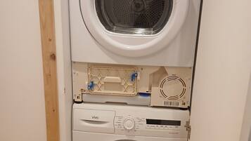 Un appareil compact combinant lave-linge et sèche-linge, doté d’un panneau de commande et d’un petit compartiment de rangement.