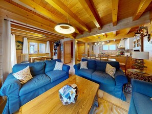 A cozy cabin interior with two blue sofas, a wooden coffee table, and a kitchen area.