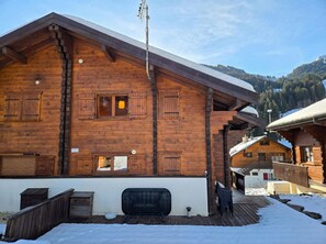 A wooden chalet with a sloped roof, a chimney, and a balcony with a metal railing.