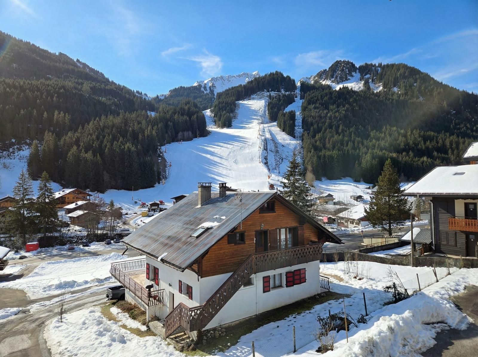 Un chalet en bois doté d’un balcon, entouré de paysages enneigés et avec une piste de ski en arrière-plan.