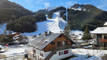 Un chalet en bois doté d’un balcon, entouré de paysages enneigés et avec une piste de ski en arrière-plan.