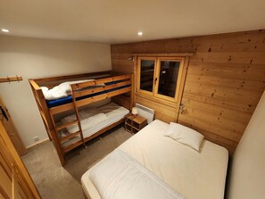 A bunk bed room with a window, a bedside table, and a radiator.