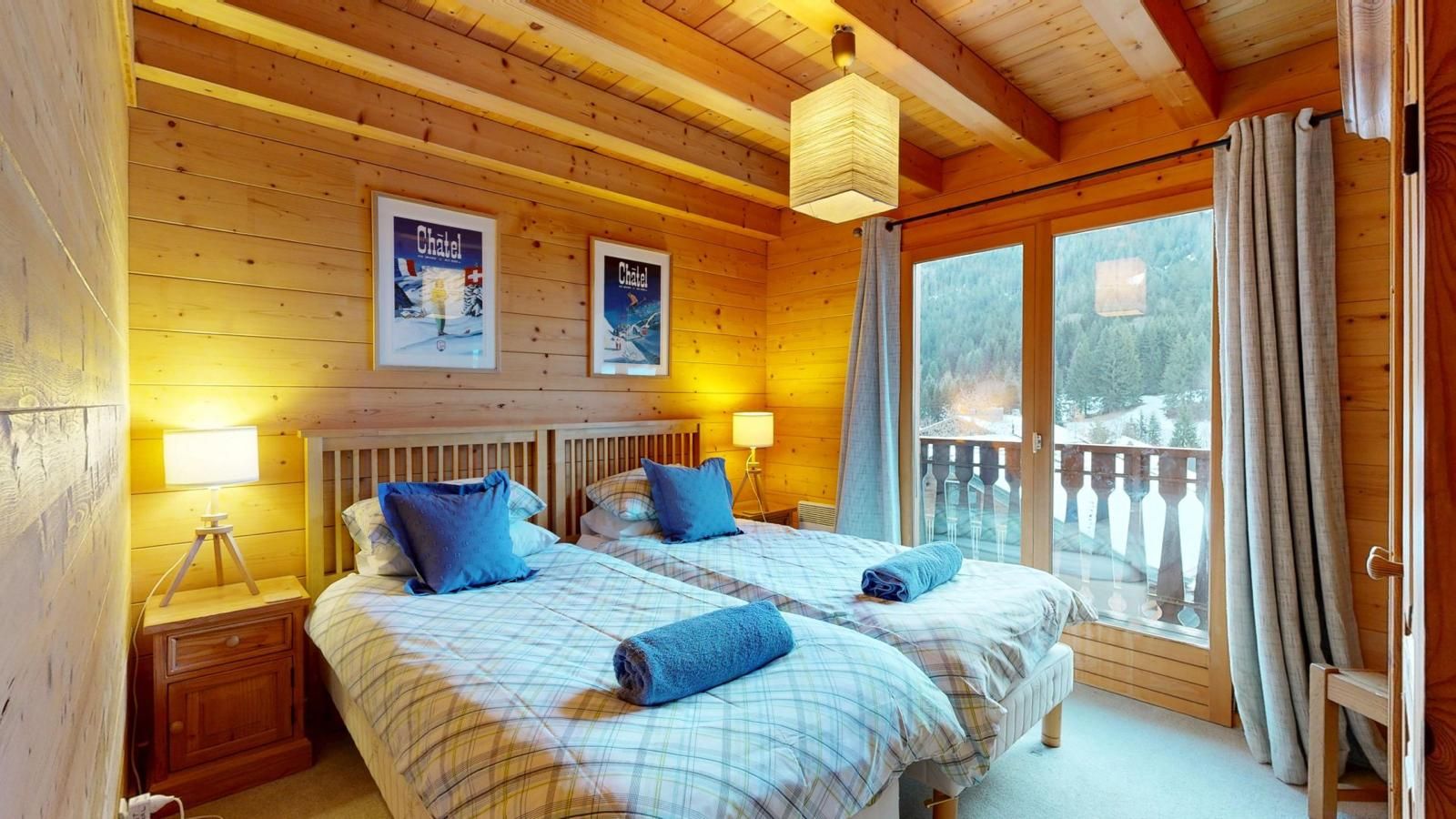 Une chambre dans un chalet en bois, avec deux lits, une fenêtre donnant sur un paysage agréable et un balcon.