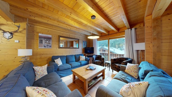 A cozy cabin interior with a wooden ceiling, a sofa set, a television, and a dining area.