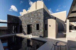 Un edificio moderno con piscina, fachada de piedra y zona de estar al aire libre.