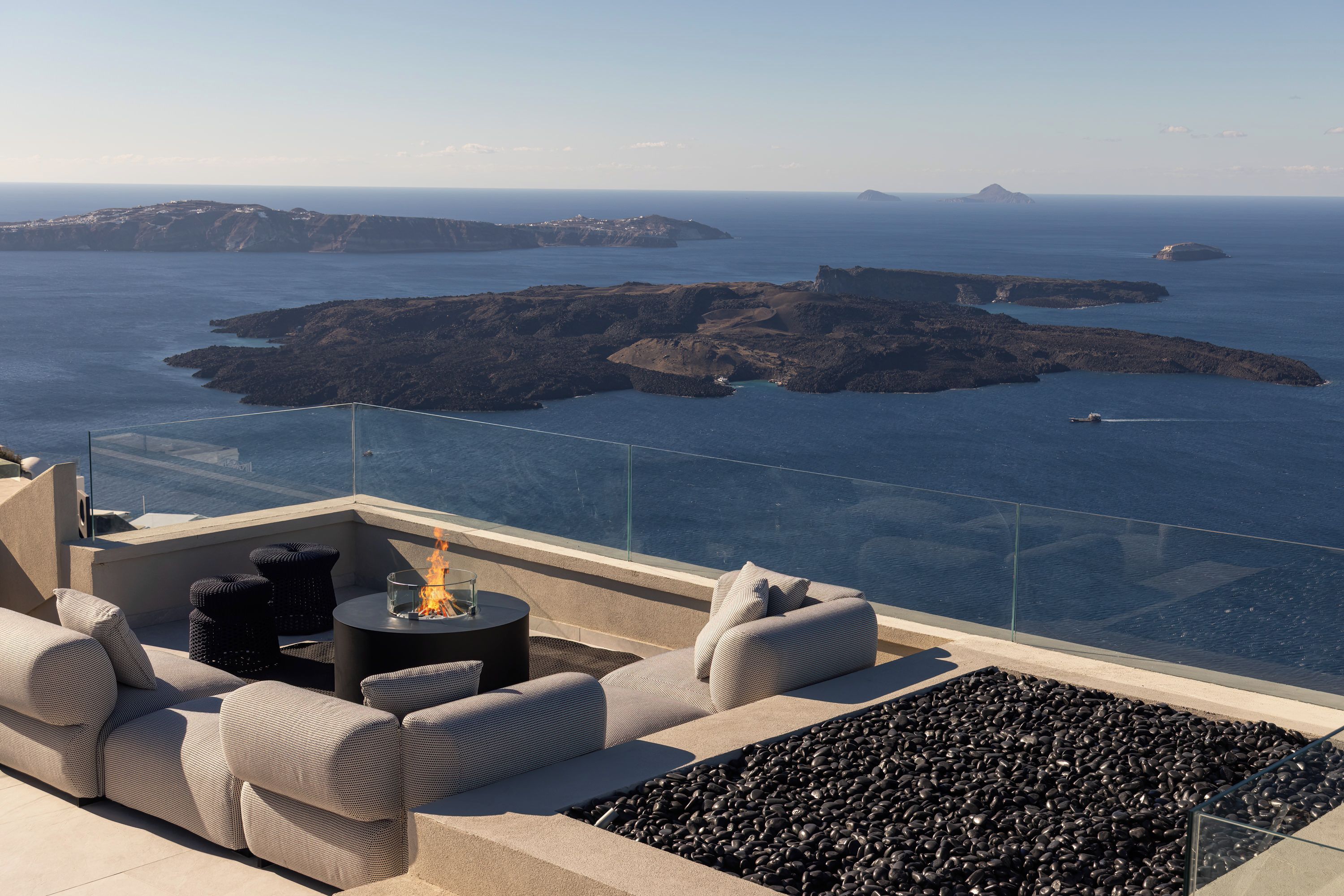 Una terrazza con posti a sedere all'aperto e un elemento decorativo a fuoco, con vista su un paesaggio costiero e isole.