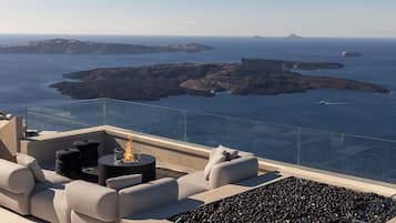 Una terrazza con posti a sedere all'aperto e un elemento decorativo a fuoco, con vista su un paesaggio costiero e isole.