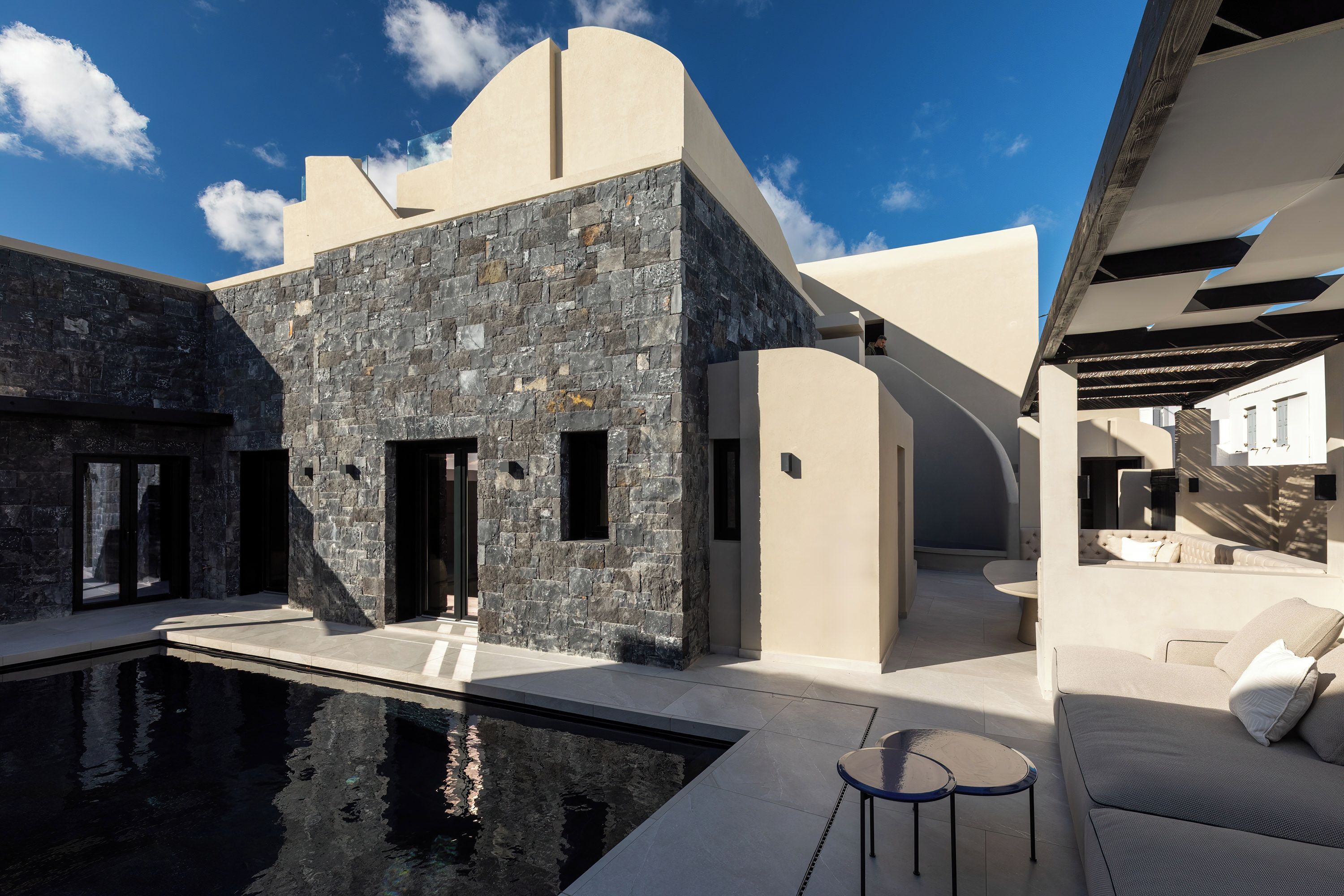 A modern building with a pool, stone facade, and outdoor seating area.