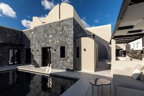 Un bâtiment moderne doté d’une piscine, d’une façade en pierre et d’un espace extérieur aménagé pour s’asseoir.
