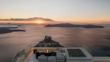 Ein moderner Außenbereich mit Feuerstelle, der einen ruhigen See und entfernte Inseln im Sonnenuntergang überblickt.