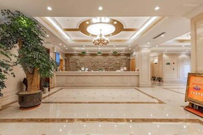 Un vestíbulo de hotel con una recepción, una araña y una gran planta en maceta.