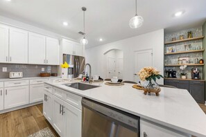 A modern kitchen with white cabinetry, a stainless steel refrigerator, and a dishwasher. - Brand New Family 6BR Pool Spa Game Lounge 7875 (Kissimmee)