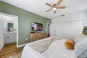 Ein Schlafzimmer mit einem Bett, einem Deckenventilator, einem Fernseher und einer Kommode.