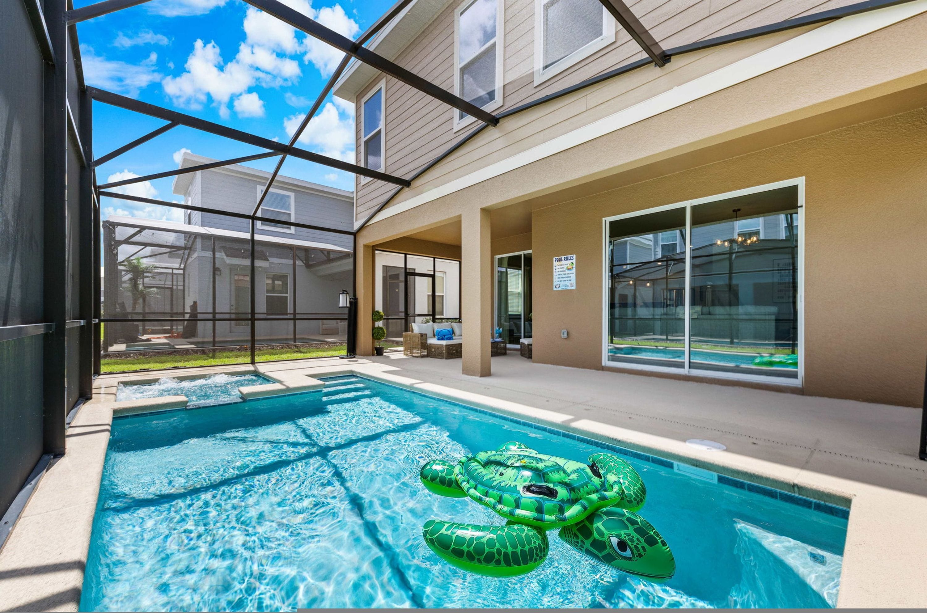 Une piscine avec un grand flotteur en forme de tortue gonflable verte, entourée d’une terrasse couverte d’où l’on peut admirer un quartier résidentiel.