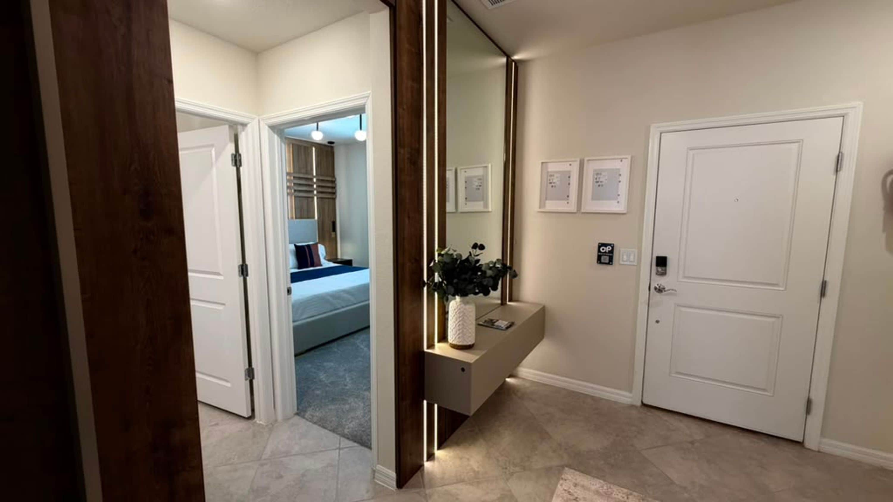 A hallway with a bed, a mirror, a plant, and a door.