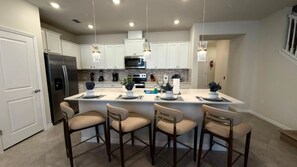 Una cocina moderna con armarios blancos, un refrigerador de acero inoxidable, una isla central con taburetes y iluminación colgante.