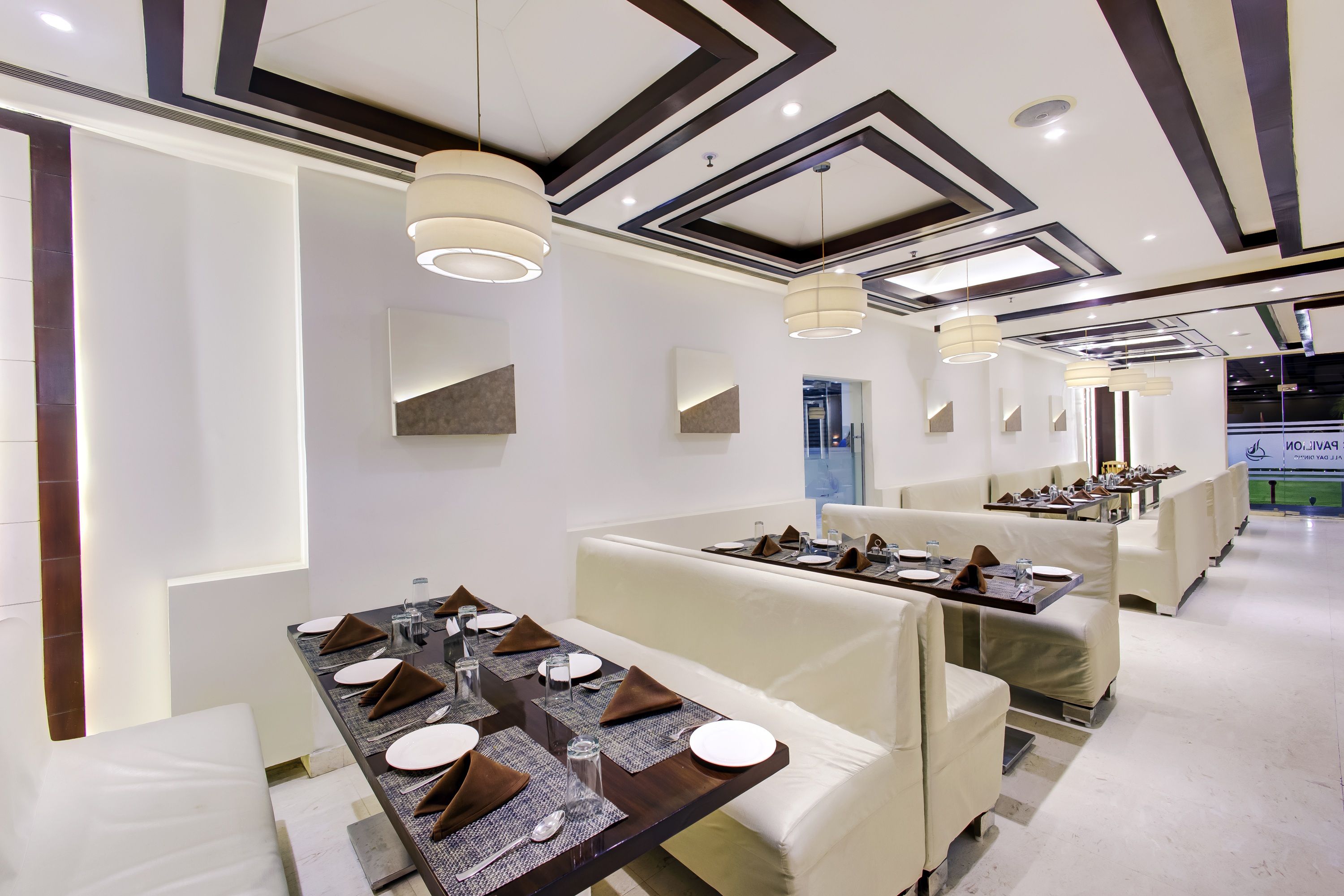 Un comedor moderno con mesas altas, asientos tipo banca acolchados e iluminación colgante.