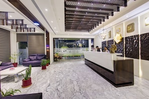 Un lobby moderno de hotel con recepción, zona de estar y elementos decorativos.