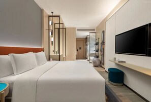 A hotel room with a large bed, a TV, a desk, and a seating area.