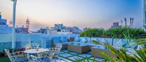 A rooftop terrace with outdoor furniture, a view of the city skyline, and a mosque with a dome.