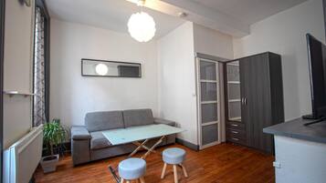 Un espace de vie moderne comprenant un canapé gris, une petite table, deux tabourets, un miroir et une armoire.
