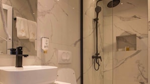 A modern bathroom with a white sink, toilet, and glass-enclosed shower area. - Plaza Boutique Hotel Prishtina (Pristina)