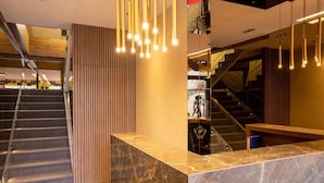 A hotel lobby with a marble reception desk, a staircase, and a modern light fixture. - Plaza Boutique Hotel Prishtina (Pristina)