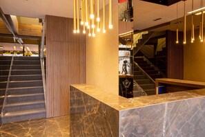 Een hotel lobby met een marmeren receptiebalie, een trap en een modern verlichtingsarmatuur.