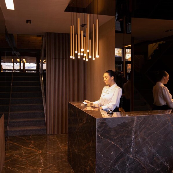 A reception desk with a marble counter, a modern pendant light fixture, and a staircase in the background. - Plaza Boutique Hotel Prishtina (Pristina)
